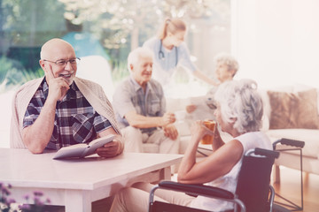 Wall Mural - Elderly woman in the wheelchair drinking tea while talking with smiling senior man