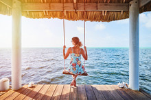 A Woman Sitting On A Swing Looking At The Ocean.