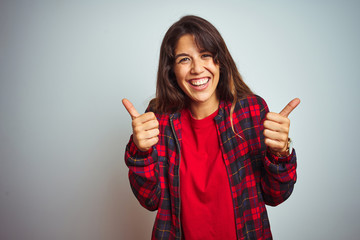 Young beautiful woman wearing red t-shirt and jacket standing over white isolated background success sign doing positive gesture with hand, thumbs up smiling and happy. Cheerful expression