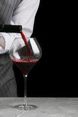 Wall Mural - bartender pours wine in glass on dark background