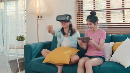 Wall Mural - Young Lesbian lgbtq Asian women couple using tablet at home, Asian lover female feeling happy fun and virtual reality, VR playing games together while lying sofa in living room at home concept.