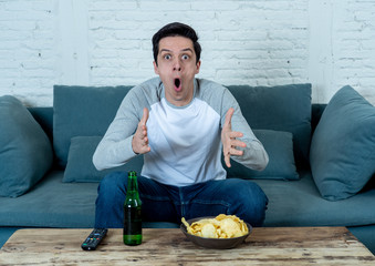 Wall Mural - Excited young man sitting on the couch watching football. Sports supporters and fans concept