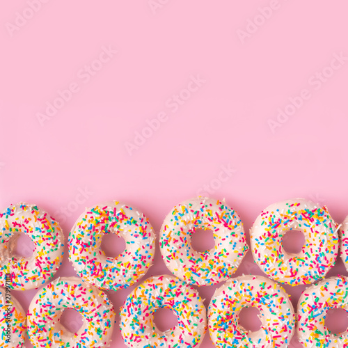 festive background of donuts with sprinkles and icing over pink background, c...
