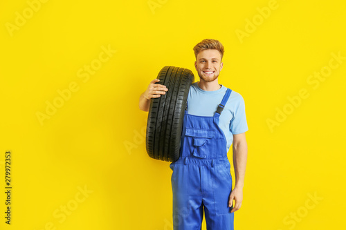 Obraz Dibond Young male mechanic with car tire on color background