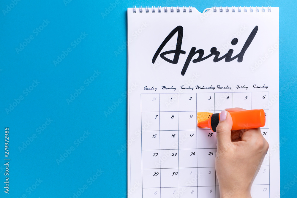 Woman marking date in calendar on color background