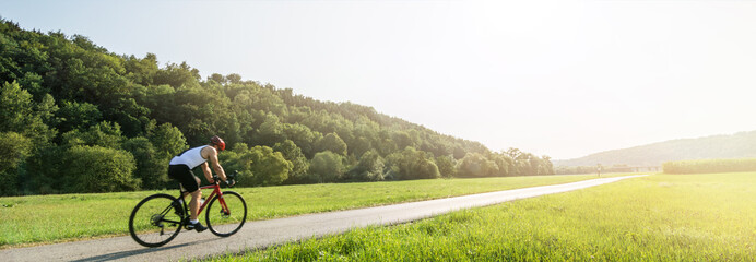 Panorama shot of cyclist on racing cycle in a rural landscape in summer with scenic lens flare