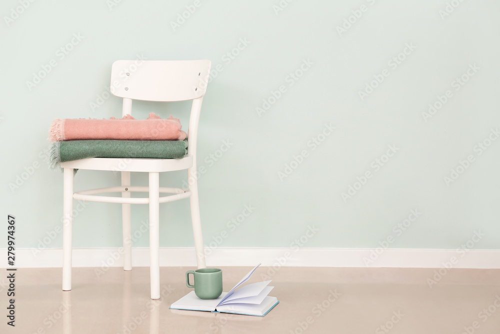 Chair with plaids and book with cup on floor near light wall