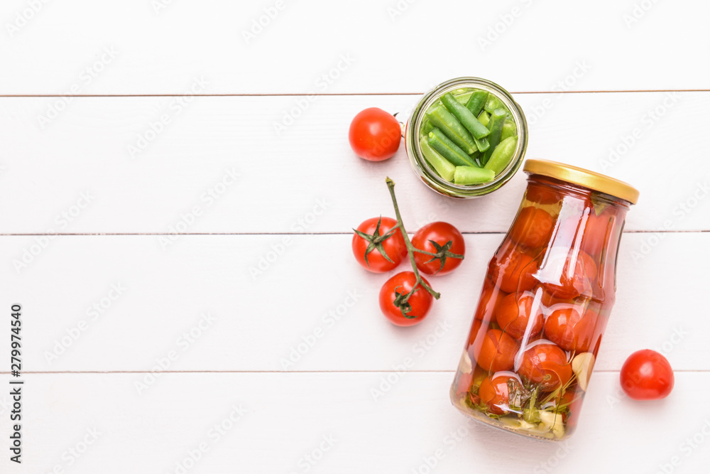 Jars with different canned vegetables on white wooden background