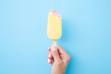 Young Woman Hand Holding Pink Ice Cream With White Chocolate Glaze On Pastel Blue Background. Bitten Food. Closeup.