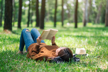 A Beautiful Asian Woman Lying And Reading A Book In The Park