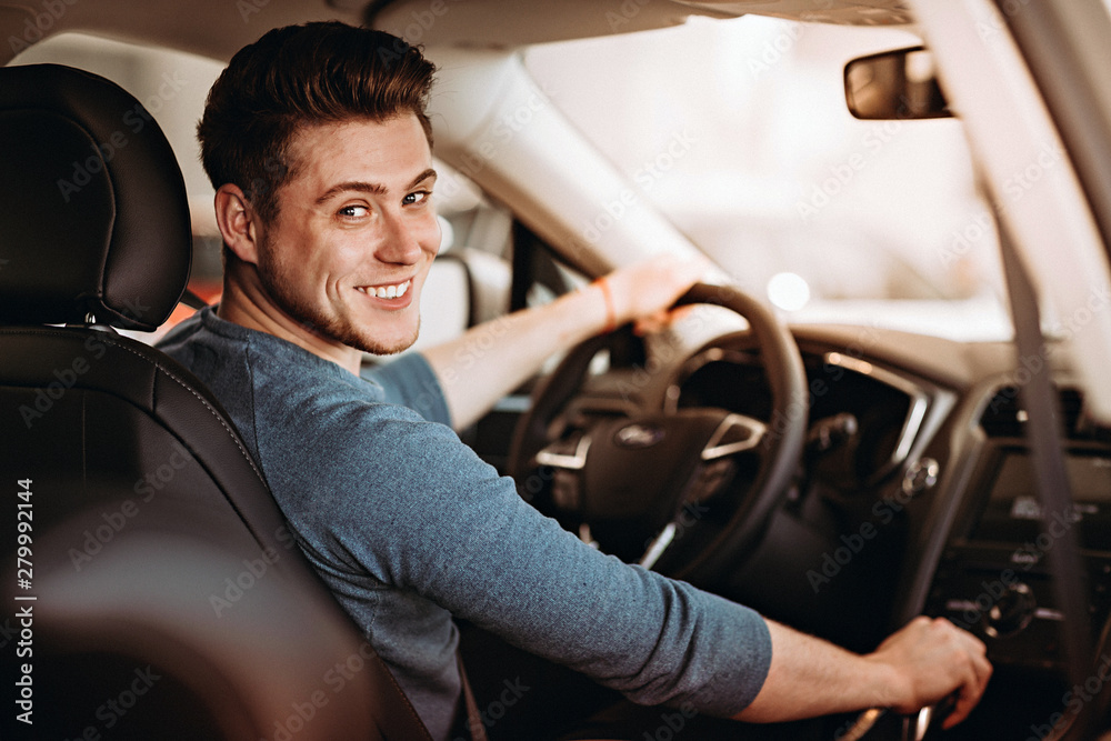 Happy young driver behind the wheel of a car. Buying a car and driving concept. - obrazy, fototapety, plakaty 