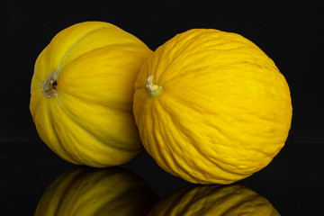 Group of two whole ribbed fresh yellow melon canary isolated on black glass