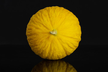 One whole bright fresh yellow melon canary isolated on black glass