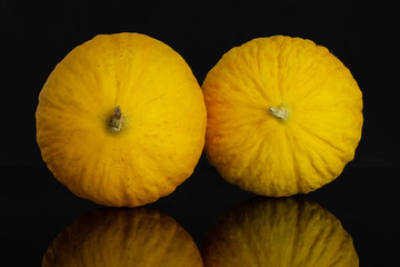 Group of two whole fresh yellow melon canary isolated on black glass