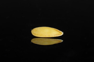 One seed of fresh yellow melon canary isolated on black glass
