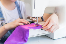 Seamstress Sits And Sews On A Sewing Machine. The Seamstress Work On The Sewing Machine. The Tailor Makes Clothes At His Workplace. Hobby Sewing As A Small Business Concept. Dressmaker