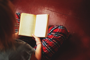 Wall Mural - a girl in plaid pants reading a book on the floor by the window