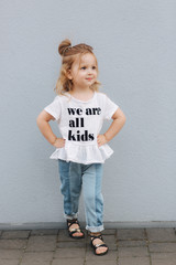 Beautiful little girl dressed in white shirt and jeans stand in front of gray wall. happy children