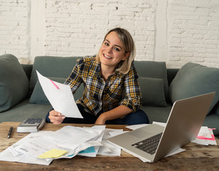 Close up of happy young woman sitting on the sofa surrounded by papers calculating and paying bills