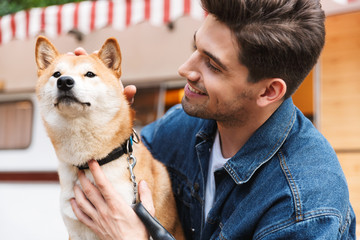 Wall Mural - Portrait of happy smiling man wearing denim clothes petting red dog near house on wheels outdoors