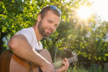 Summertime In Garden. Young Man Is Playing Acoustic Guitar In The Garden At Sunset.