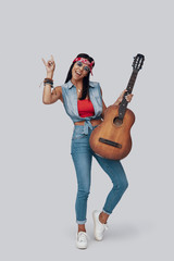 Canvas Print - Full length of attractive stylish young woman carrying acoustic guitar and smiling while standing against grey background