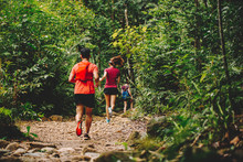 Runners. Young People  Trail Running On A Mountain Path. Adventure Trail Running On A Mountain. Athletic Attractive People Running Enjoying The Sun Exercising Their Healthy Lifestyle.