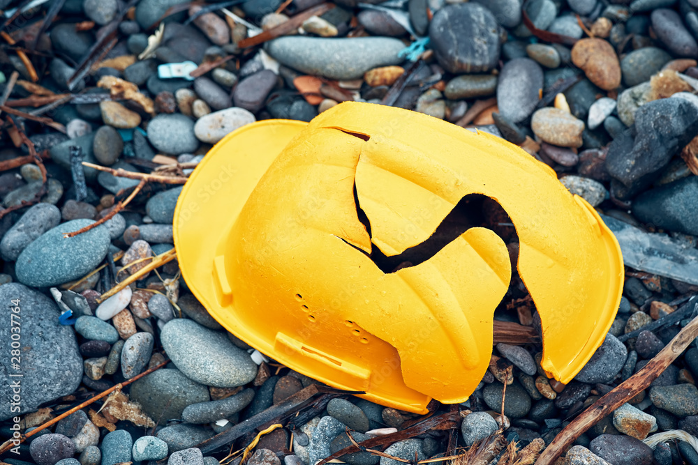 Cracked work helmet on the floor covered with pebble stones. Concept of work accident. - obrazy, fototapety, plakaty 