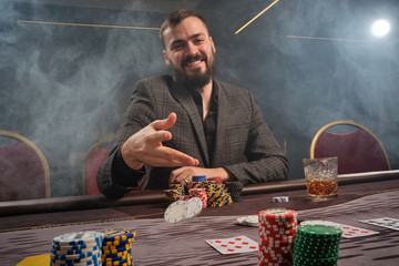 Handsome bearded man is playing poker sitting at the table in casino.