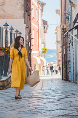 Wall Mural - young pretty woman in yellow dress walking by small porec city streets sea on background