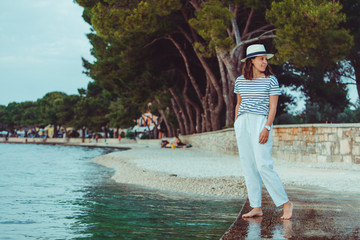 Wall Mural - woman in white clothes and fedora hat walking by sea beach