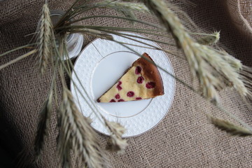 Wall Mural - Raspberry cake piece on white plate with background of  sackcloth and spikelet