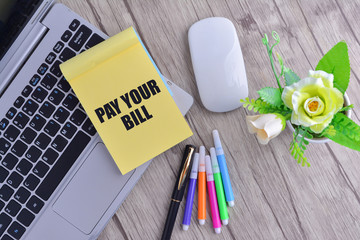 Laptop, notebook with magnifying glass on wooden table with text Pay Your Bill