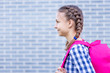 Beautiful student teenager schoolchild with backpack looking away. Smiling cute child with bag. Teen girl with braided hair against a brick wall outdoors. Childhood and Back to school concept.