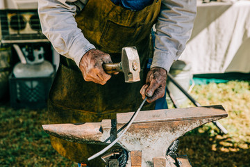 A tradesman with an apron on hammering a hot piece of iron, molding it into a shape for his hobby craft. blacksmith