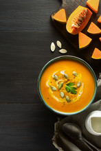 Pumpkin Cream Soup In A Bowl With Pumpkin Seeds, Parsley, Cream And Fresh Orange Butternut Squash Slices On Wood. Traditional Fall, Thanksgiving Meal. Healthy Organic Vegan Food. Vertical, Top View