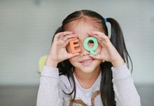 Cute Little Asian Child Girl Holding Alphabet EQ (Emotional Quotient) Text On Her Face. Education And Development Concept.
