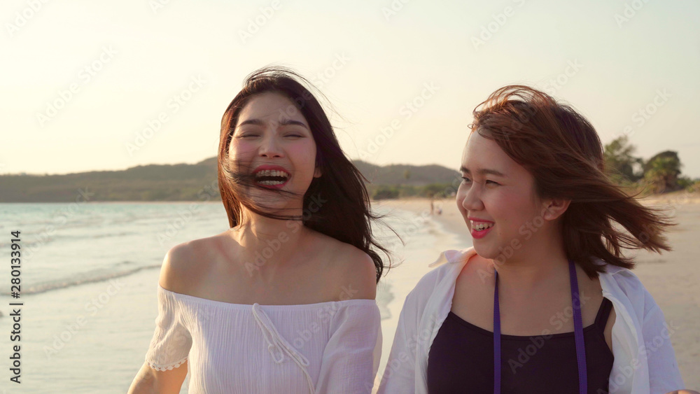 Young Asian lesbian couple walking on beach. Beautiful women friends happy relax walking on beach near sea when sunset in evening. Lifestyle lesbian couple travel on beach concept.