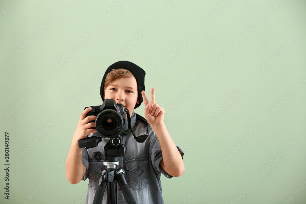 Cute little photographer with professional camera on color background