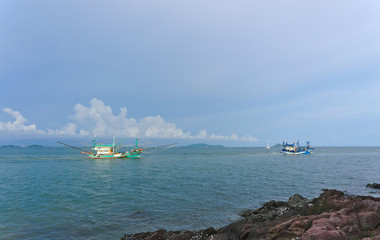 Fishing ship fleet passing the shore and lighthouse going to work in the deep sea looking for seafood such as fish crabs shrimps and squids in the evening with beautiful clouds and sky