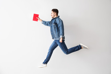 Jumping young man with book on light background