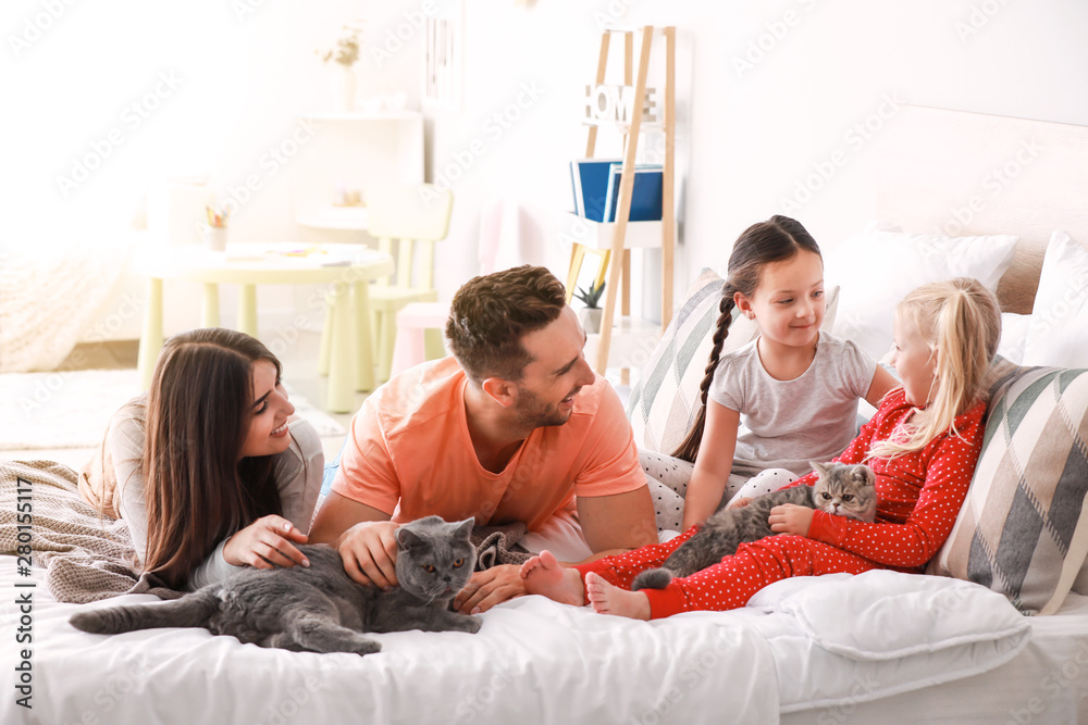 Happy family with cute cats on bed at home