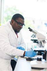 African-american scientist working in lab. Doctor making microbiology research. Laboratory tools: microscope, test tubes, equipment. Biotechnology, chemistry, bacteriology, virology and health care.