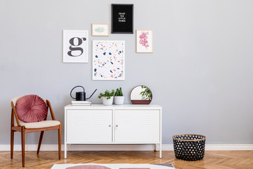 Design scandinavian home interior of open space with mock up posters gallery wall, white shelf, stylish chair, plants and elegant accessories. Gray background walls. Retro cozy home decor. Template.