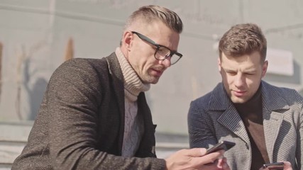 Sticker - Two beautiful adult men communicate using smartphones while sitting outside