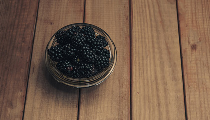 Poster - Fresh blackberry in glass bowl on a brown wooden table background.