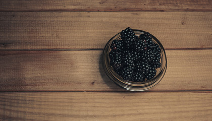 Poster - Fresh blackberry in glass bowl on a brown wooden table background.