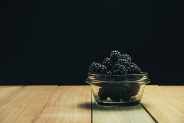 Poster - Fresh blackberry in glass bowl on a brown wooden table background.