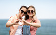 © Syda Productions - leisure and friendship concept - happy smiling teenage girls or best friends in sunglasses at seaside in summer hugging and making hand heart gesture