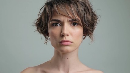 Poster - Serious young lady with natural skin becoming scared while looking at the camera over grey background isolated